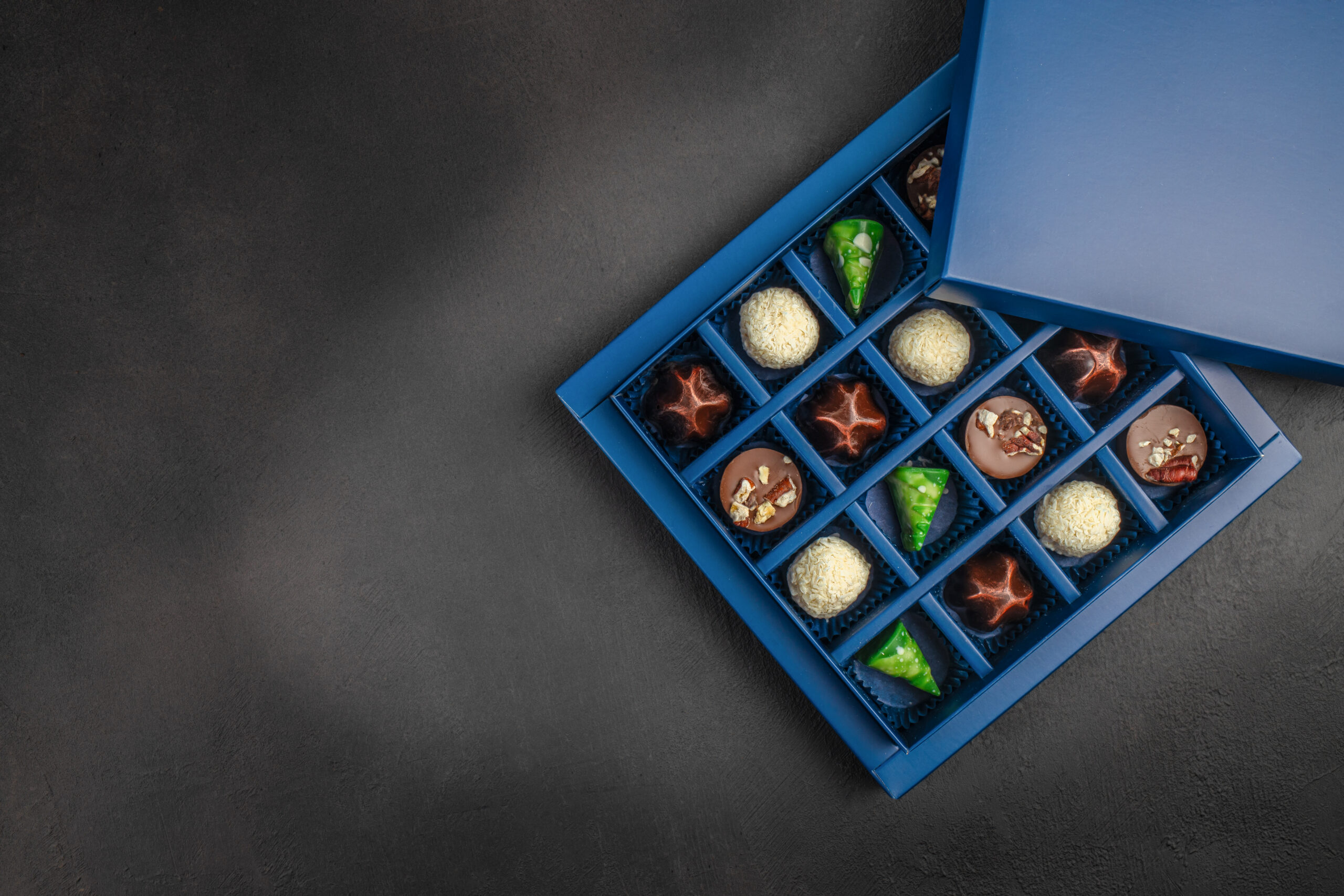 Luxury assorted chocolate pralines arranged in an elegant blue gift box on dark background with copy space, perfect for advertising, holidays and premium branding.
